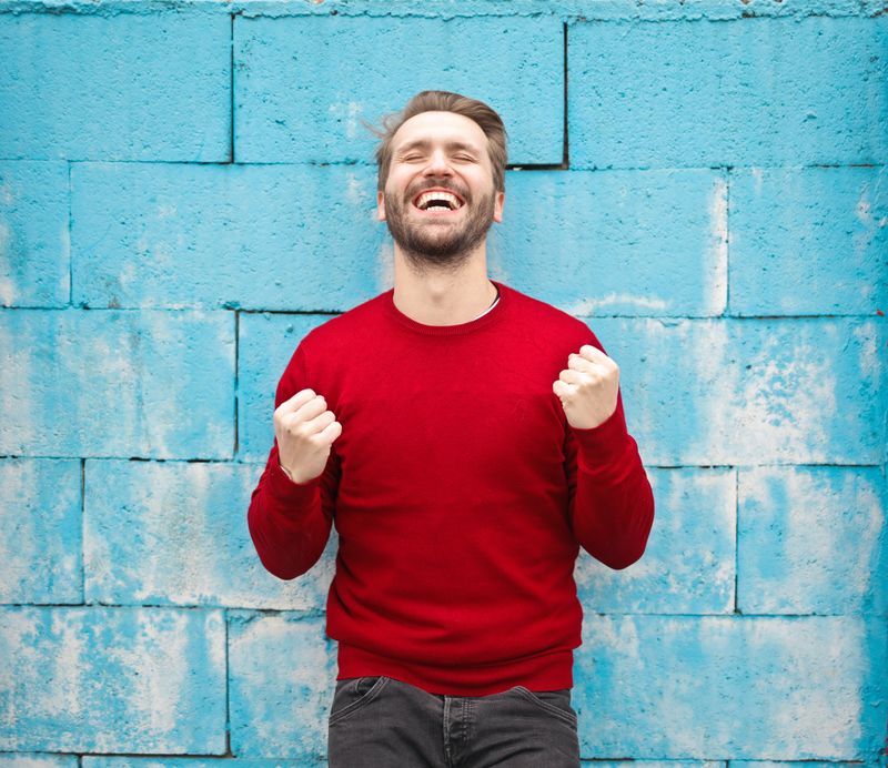 Man wearing red sweater expressing excitement and standing in front of a blue brick wall