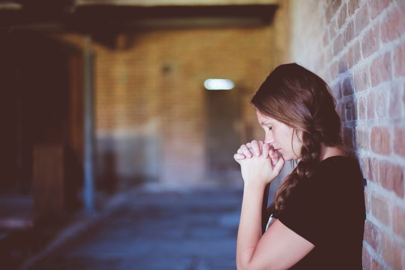 A women takes a moment to collect herself, with her hands clasped and eyes closed.