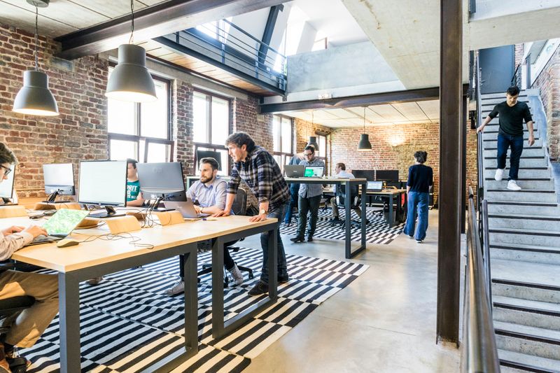 A large office space with people working on computers at big tables and standing desks.
