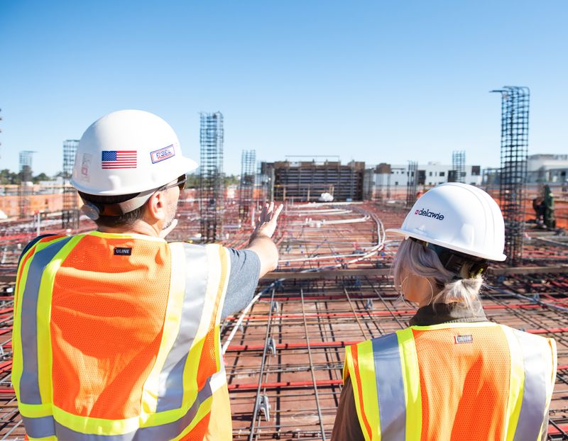 Two workers on a construction site wearing hard hats surveying a project