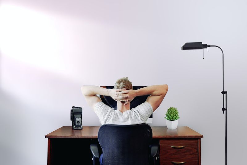 Back view of a man stretching in his chair, looking at his computer