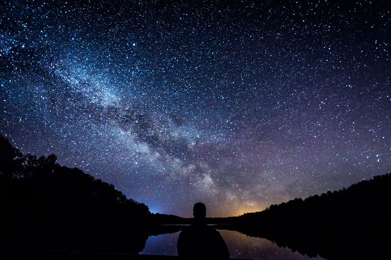 Silhouette of man in front of lake and a sky full of stars.  