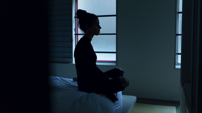 A dark picture of a woman sitting in isolation.