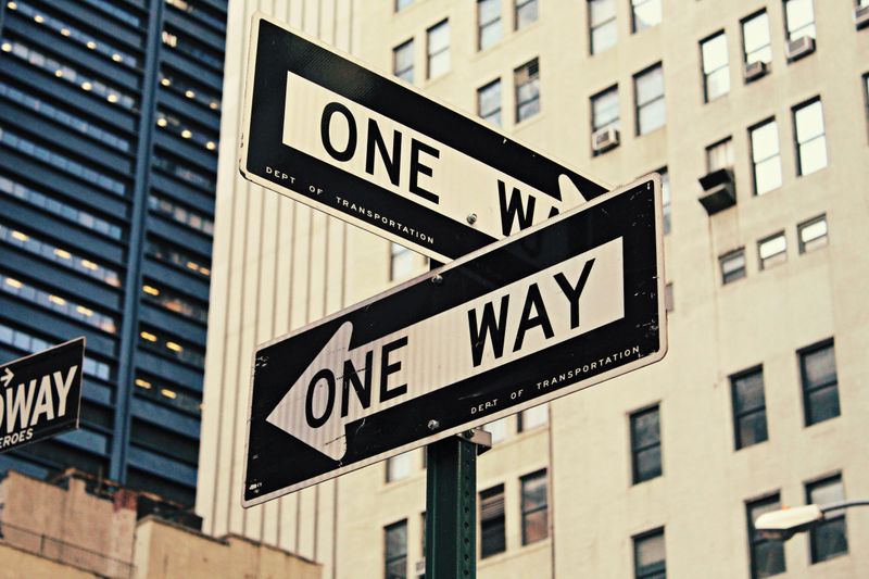 Photo of streets signs with  words "One Way" pointing at different directions.