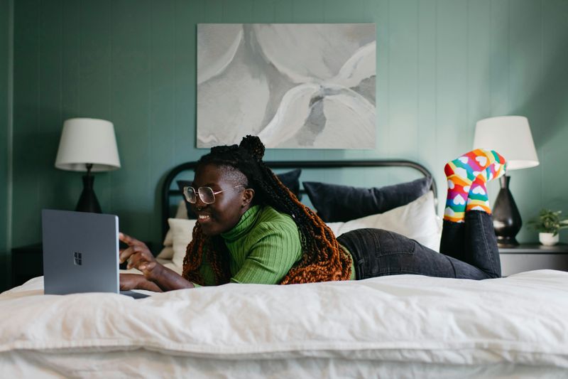 A woman laying on her stomach on a bed and using her laptop.