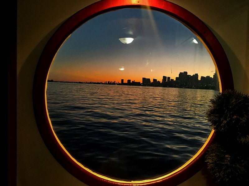 A clear round window looking out at the sea and a city skyline.