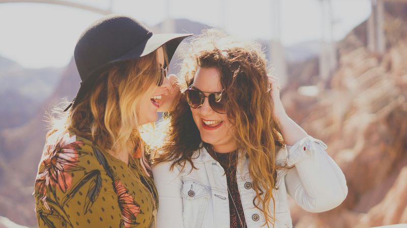 Two women chatting wearing hats and sunglasses.