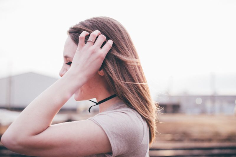 Profile of woman with straight brown hair and brown shirt holding her head