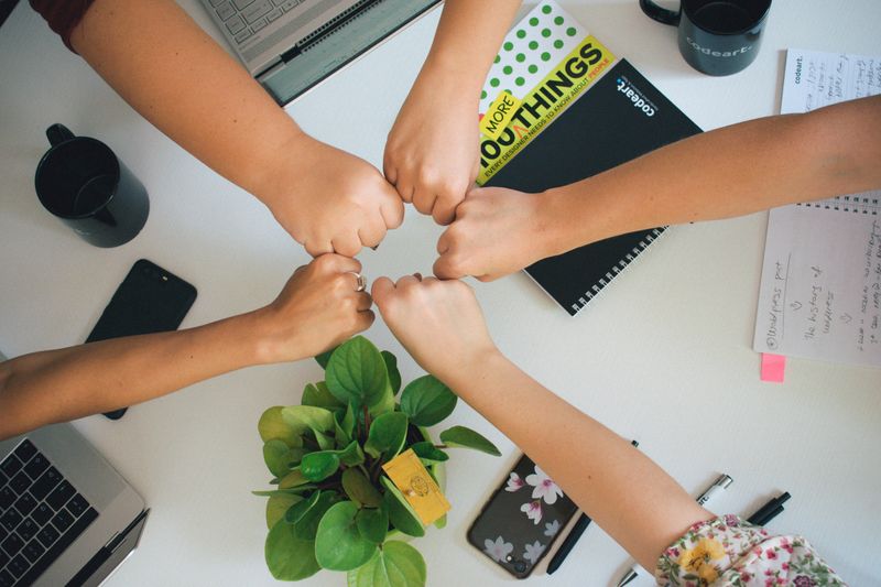A group of coworkers putting their fists together in a circle over a work desk.