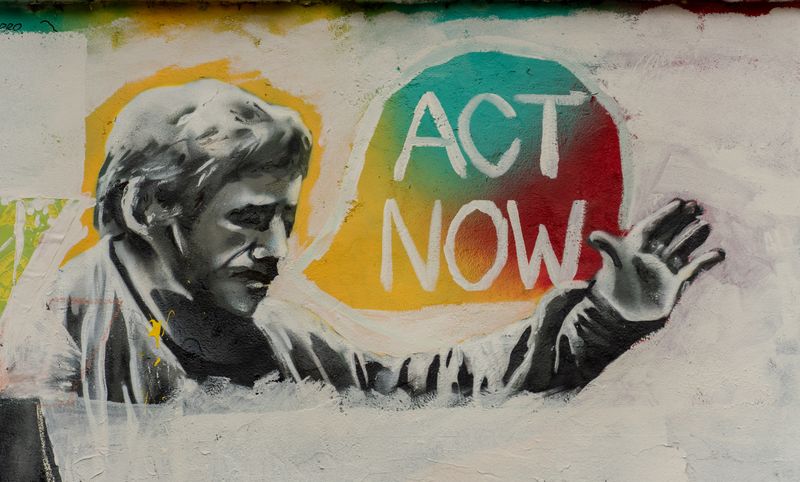 A mural of a man with a moustache. A speech bubble reads: 'Act now!'