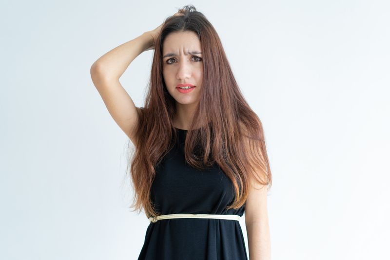 Young woman with hand raised to back of head, looking confused and distressed.