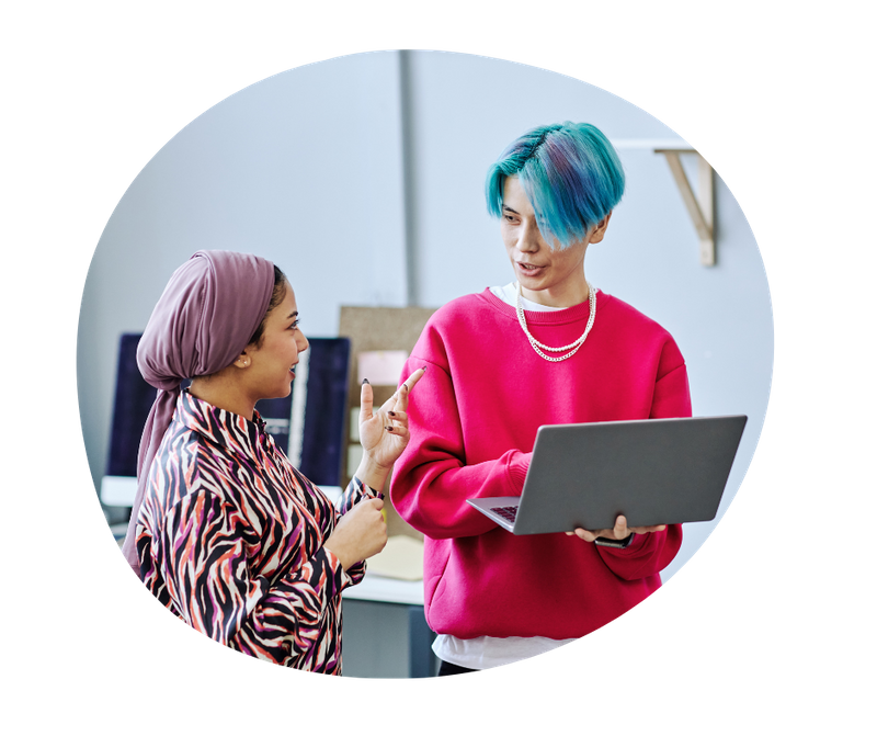 Image: Two smiling youth stand together in an office to discuss work