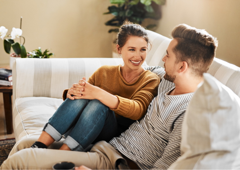 A couple sitting on a couch and talking to each other.