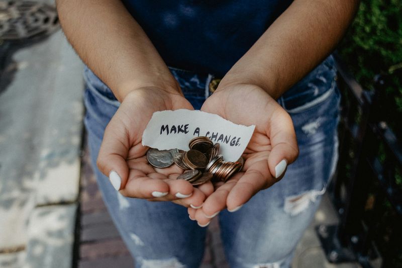 A person holding small change in their hands. A piece of paper in their hand reads: 