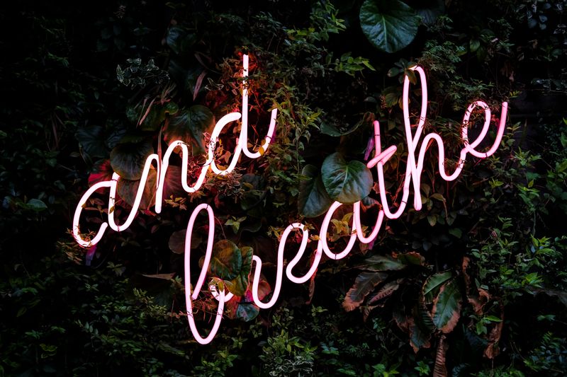 Photo of a neon sign with text 'and breathe'.