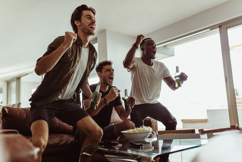 Three roommates cheering for a sports game on television