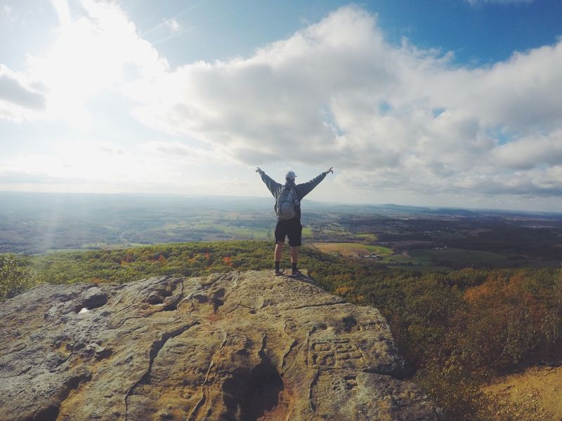 A man stands on the top on the mountain overlooking a view of trees and sky