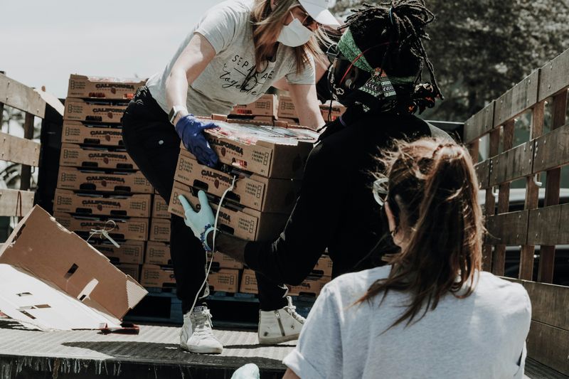 A person handing boxes of fruit to another person from the back of a truck..