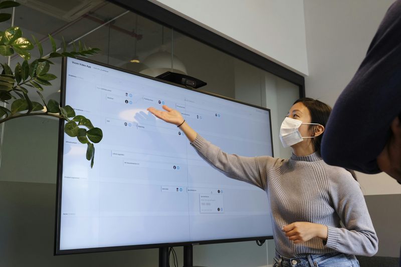 A woman wearing a face mask and pointing to content on a large screen.