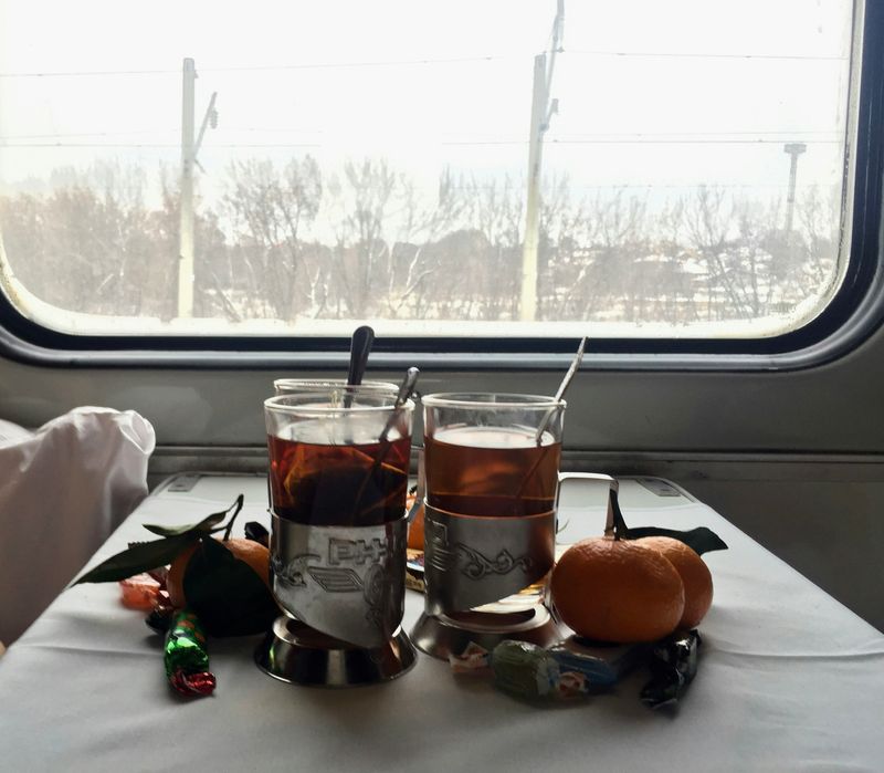 A passenger table on a train car in the winter. On the table are tea glasses and oranges.