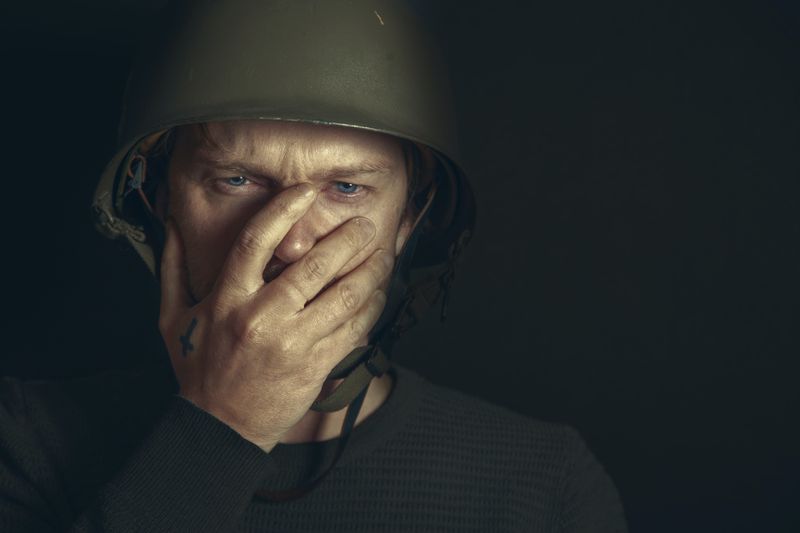 Soldier covering his mouth with his hand. Looking horrified.
