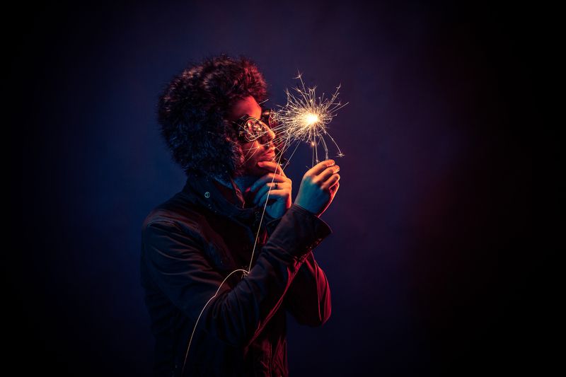 a man in a dark room holding and observing a sparkler firework.