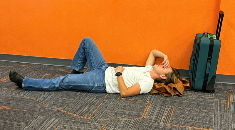 A person lying on the floor in an airport looking stressed and tired.