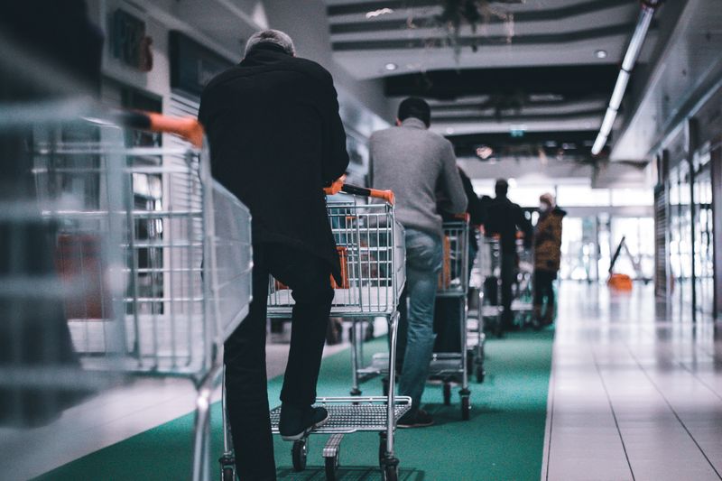 A line of customers with carts at a supermarket.  Photo by Adrien Delforge on Unsplash