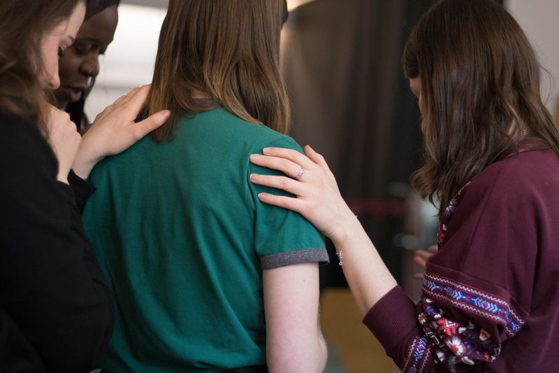 A group of people standing with their hands touching the shoulder of another person in the centre