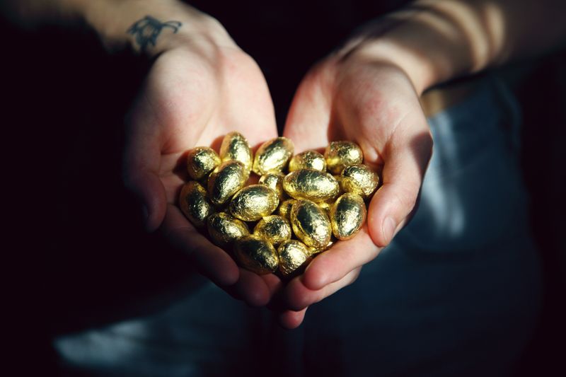 A person holding a handful of gold-foil wrapped chocolate eggs.