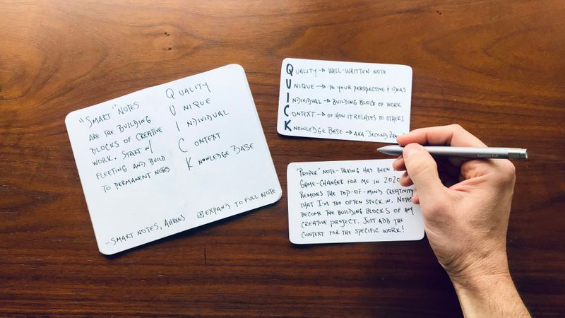 A person taking notes on three notecards on a wooden table