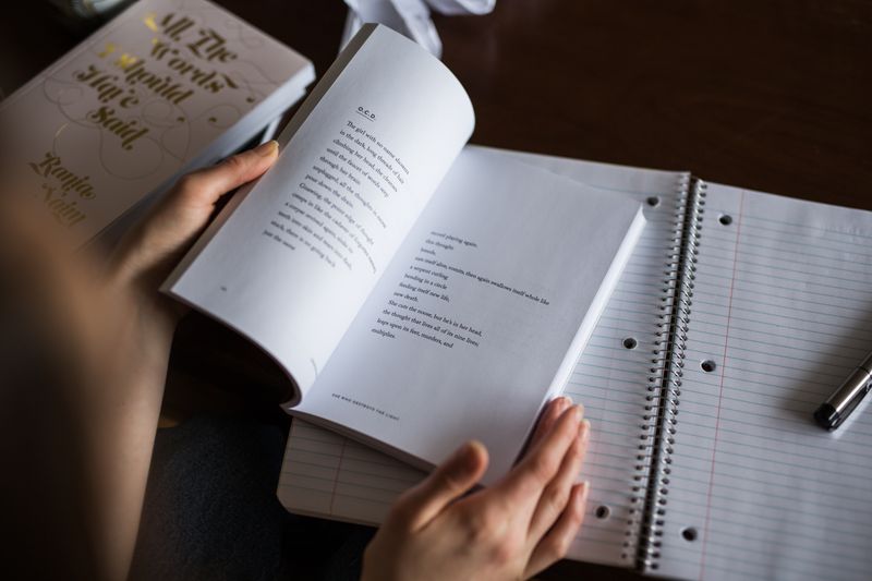 An open poetry book laying on top of an open notebook and pen.