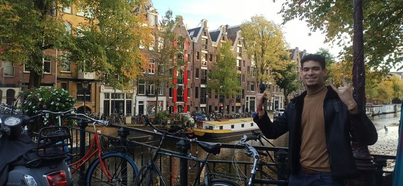 A happy person standing on a bridge by an Amsterdam canal, surrounded by bicycles.