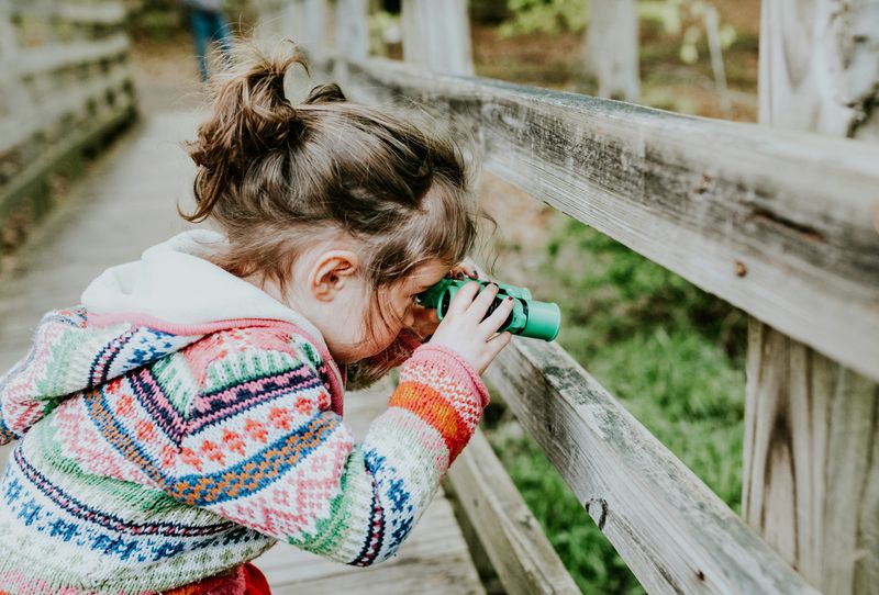 A child looking through binoculars on a wooden bridge. 