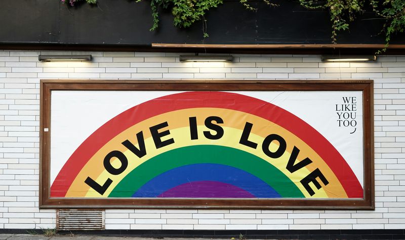 A white wall with brown picture frame that says 'Love is Love' in black letters with a rainbow background.
