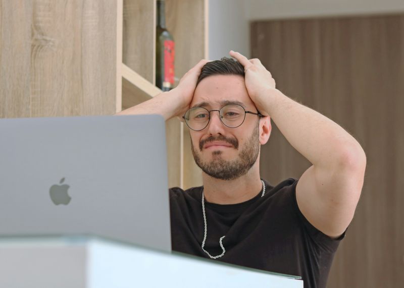 A man sitting at a laptop holding their head in frustration.