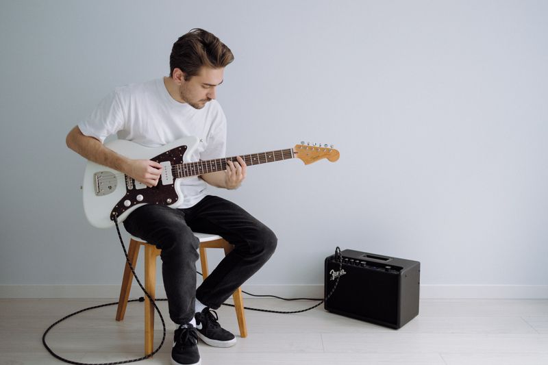 Man holding a white electric guitar that is plugged into an amplifier.