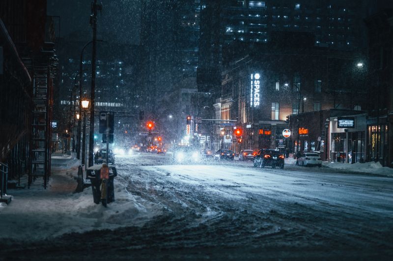 Dark, snowy street with red traffic lights in the distance.