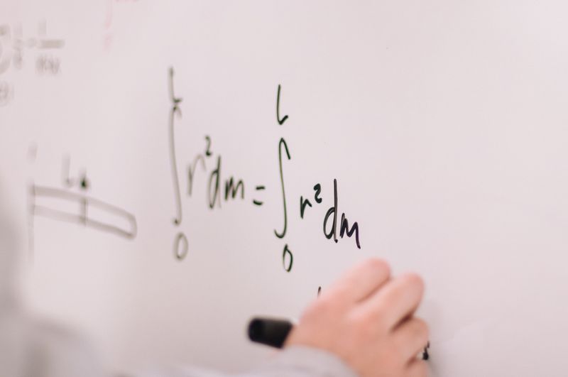 A person writing a complex equation on a white board.