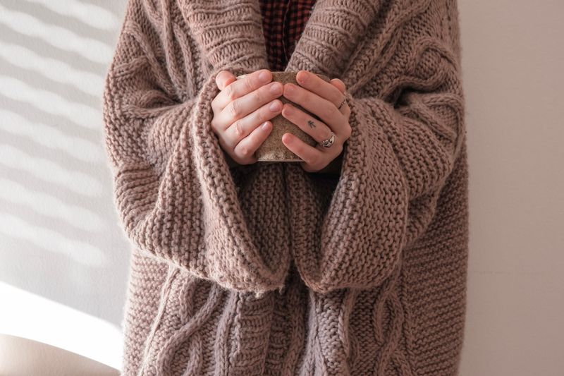 Person wearing a sweater while holding a mug