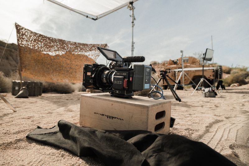 A film set in a desert location. A camera sits on top of a wooden box.