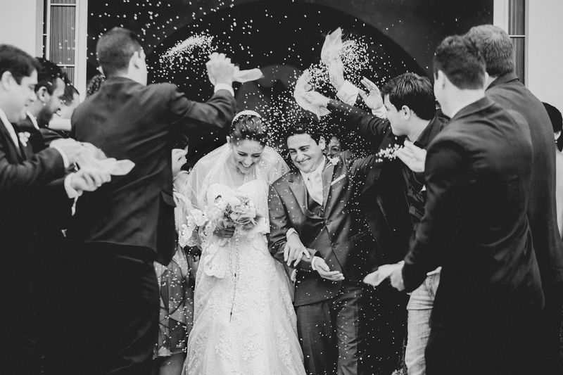 A bride and groom walking out of a wedding venue. A crowd throws rice at them in celebration.