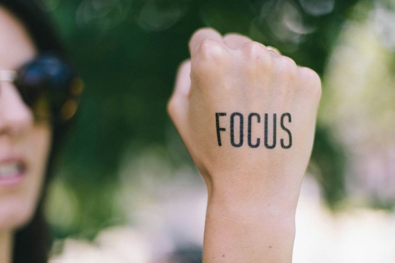 A woman holds up her first, which is tattooed with the word "Focus".