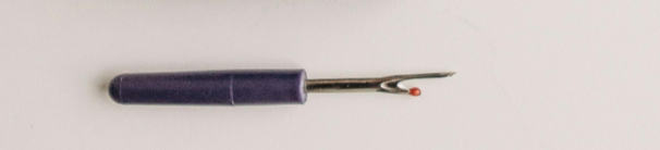 A seam wripper tool. It is a handheald tool with a two metal points, one longer than the other.