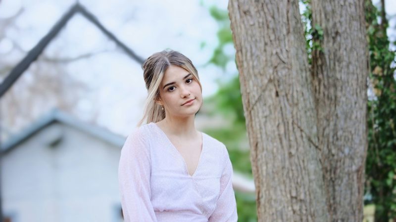 A teenage girl in pink blouse sitting outside.