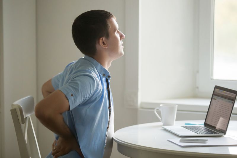 Profile portrait of man at laptop, stretching, backache position