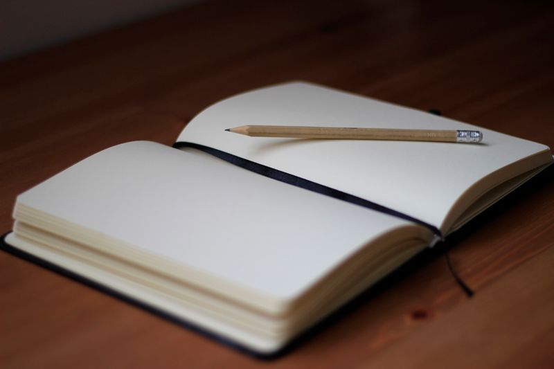 Photo of a notebook, open to a blank page, with a pencil on top