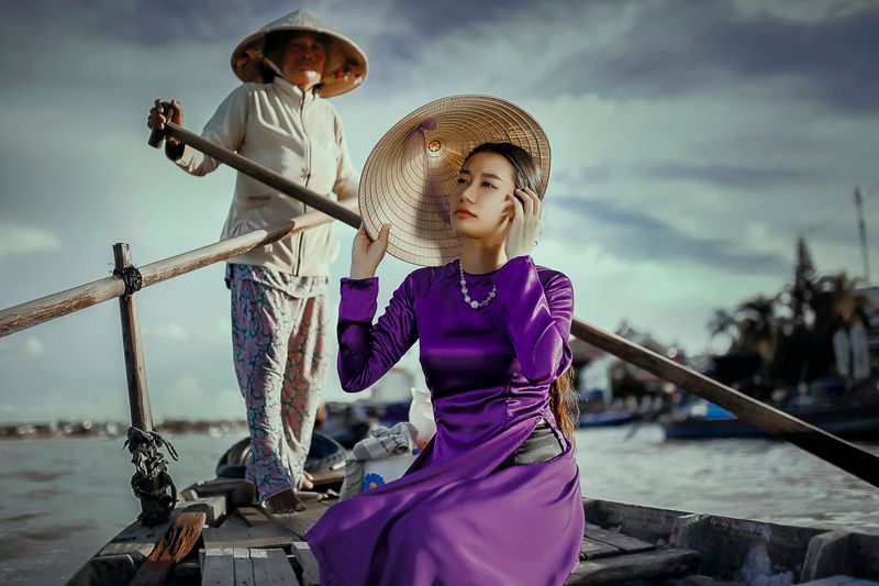 A Vietnamese woman sitting on a boat with another woman rowing the boat.