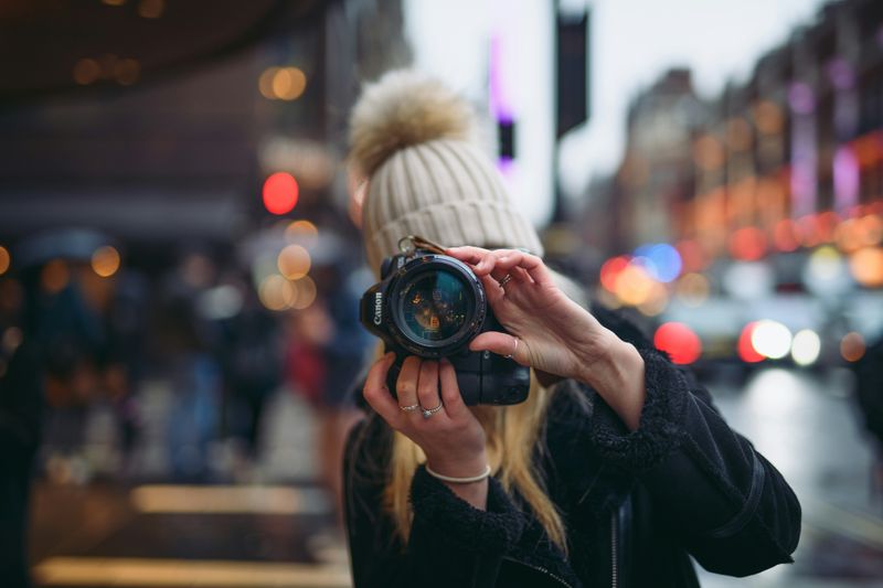 A woman pointing a digital camera down a busy street.