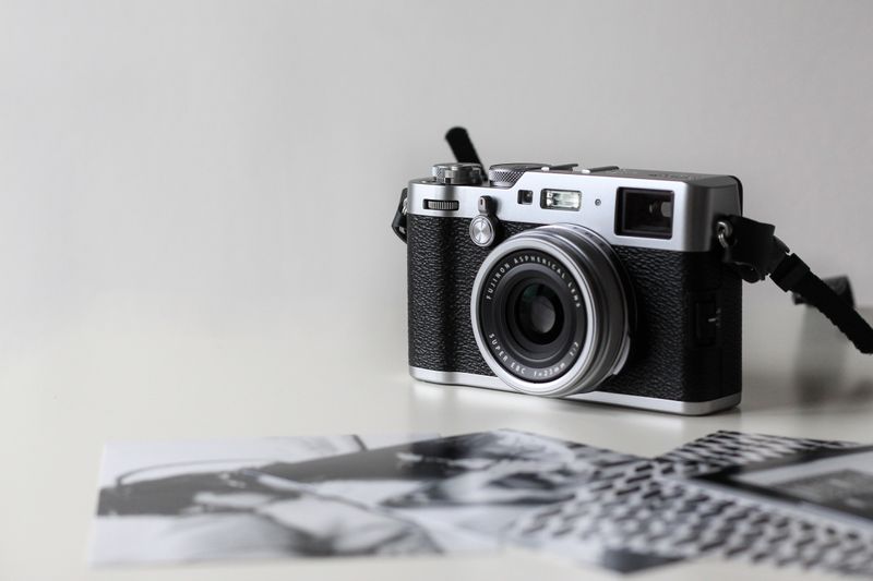 Picture of vintage camera on gray background with blurred black and white photos laying in front of the camera. 